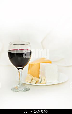 Verre avec vin rouge et fromage sur une plaque sur fond clair Banque D'Images