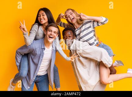 Deux couples étudiants internationaux qui s'amusent sur fond jaune Banque D'Images