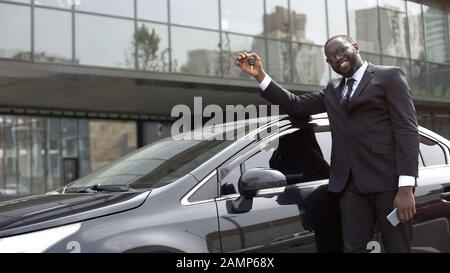 Enchanté homme africain américain montrant la clé de la nouvelle voiture de luxe, les rêves deviennent réalité Banque D'Images