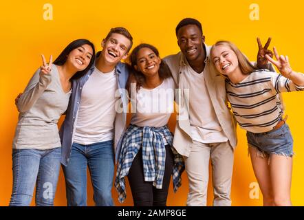 Groupe d'étudiants multiraciaux souriant et embrassant sur fond jaune Banque D'Images