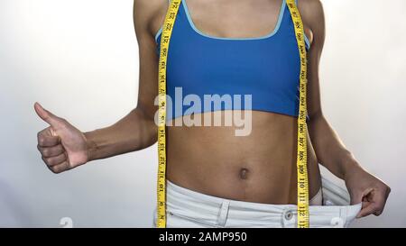 Femme de la coupe portant un pantalon surdimensionné, montrant des pouces-haut, perte de poids résultat, régime Banque D'Images