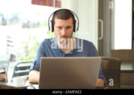 Vue avant de l'homme adulte utilisant un ordinateur portable et un casque dans un café Banque D'Images