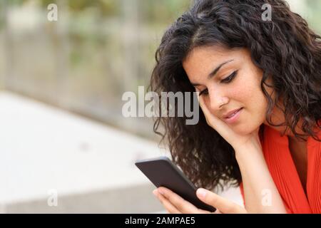 Une femme pensive qui lit des messages sur un smartphone assis dans un parc Banque D'Images