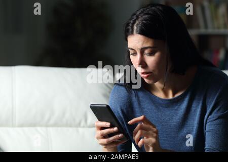 Une femme inquiète à vérifier le texte du téléphone portable assis sur un canapé dans la nuit à la maison dans la nuit Banque D'Images