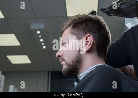 Close-up. Master coiffure blow-drys un jeune mec dans un salon de coiffure. Soins pour les cheveux des hommes. La beauté des hommes. Coupe de cheveux et de coiffure Banque D'Images