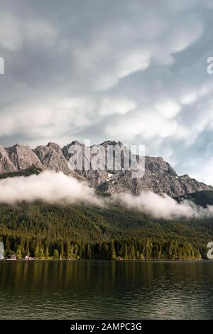 Lac d'Eibsee en face du massif de Zugspitze avec Zugspitze, nuages bas suspendus, gamme de Wetterstein, près de Grainau, Haute-Bavière, Bavière, Allemagne Banque D'Images