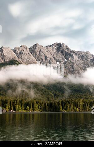 Lac d'Eibsee en face du massif de Zugspitze avec Zugspitze, nuages bas suspendus, gamme de Wetterstein, près de Grainau, Haute-Bavière, Bavière, Allemagne Banque D'Images