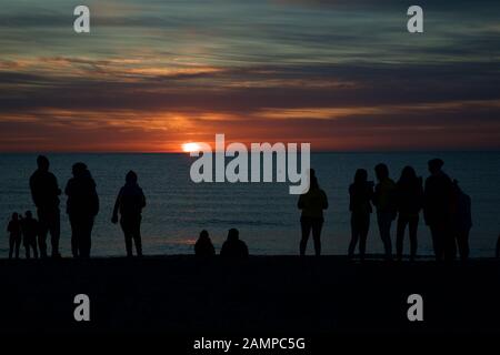 Un groupe de personnes en silhouette sur une plage, dans le comté de Wicklow, au coucher du soleil sur la côte est de l'Irlande. Banque D'Images