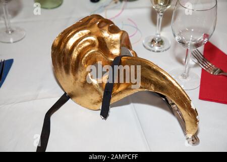 Masque de balle en mascarade doré sur une table de dîner. Carnaval Venetian Eye Mask, accessoire de robe fantaisie, boule de costume de fête de Carnaval. Banque D'Images