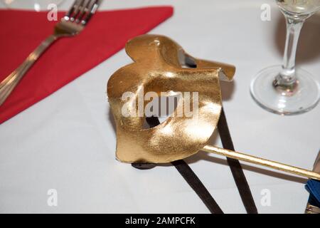 Masque de balle en mascarade doré sur une table de dîner. Carnaval Venetian Eye Mask, accessoire de robe fantaisie, boule de costume de fête de Carnaval. Banque D'Images