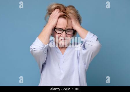 Femme âgée pensive dans des verres tenant main à son front ayant migraine ou mal à la tête. Studio tourné Banque D'Images