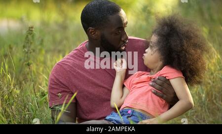 Drôle de père et de fille à faire des visages stueux ensemble, assis dans l'herbe verte Banque D'Images