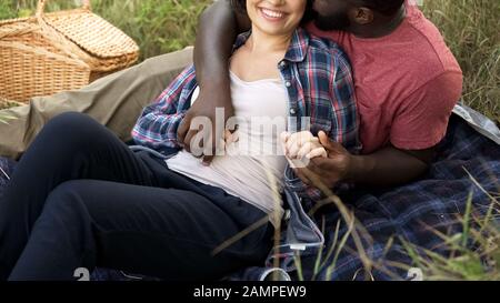 Un mari joyeux embrassant la femme enceinte à l'extérieur, les futurs parents se détendant dans la nature Banque D'Images