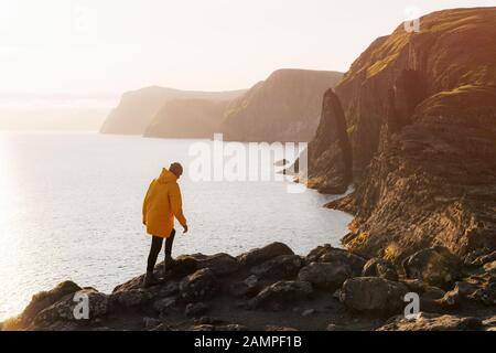 Le touriste en veste jaune regarde les falaises près du lac de Sorvagsvatn sur l'île de Vagar, îles Féroé, Danemark. Photographie de paysage Banque D'Images
