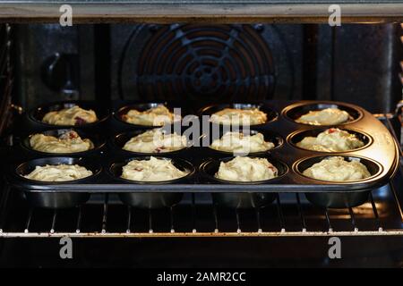 Pâte pour de délicieux muffins à la vanille végétalienne mettre dans une poêle noire dans un four éclairé - vue inclinée, format horizontal Banque D'Images