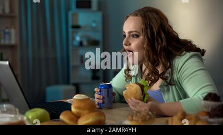 Une grosse fille étonnée regardant l'ordinateur portable, surprise par les nouvelles, manger de la nourriture de la jonque Banque D'Images