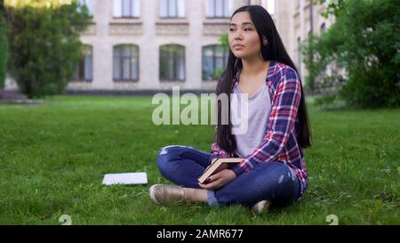 Belle jeune fille mixte assise sur pelouse près de l'université et rêvant vers la date Banque D'Images