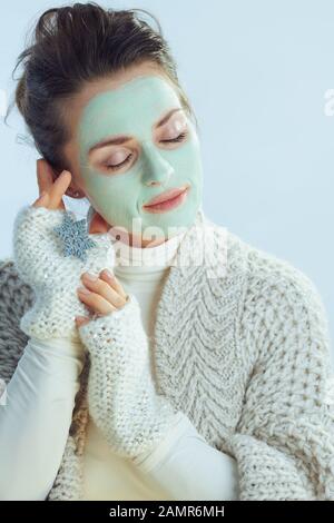 décontracté, femme de ménage de 40 ans, pull à col roulé et gilet avec masque facial vert tenant des flocons de neige isolés en bleu clair d'hiver. Banque D'Images