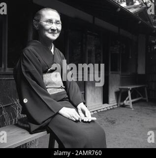 Années 1960, historiques, personnes âgées japonais assis dehors sur un banc, vêtu d'un Kimono, le costume traditionnel du Japon. Normalement à partir de la soie, ils ont de grands manches, descendre des épaules aux talons et il est détenu par un obi, une large ceinture. Banque D'Images