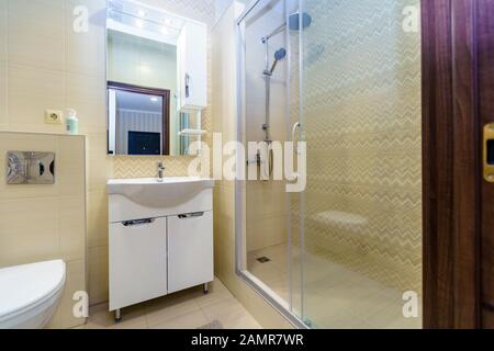 Salle de bains dans l'appartement. Douche, lavabo avec miroir, toilettes. Les carreaux de céramique carré sous la forme de modèles de robe blanche et jaune sur le mur Banque D'Images