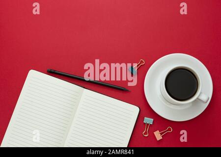 Plateau de table, bureau avec cahier ouvert et tasse à café sur fond rouge. Espace de copie pour le texte. Banque D'Images