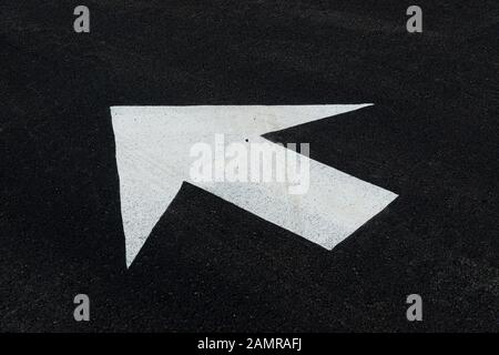 Gros plan horizontal d'une flèche blanche sur un parking noir pointant vers le coin supérieur gauche de l'image. Espace de copie. Banque D'Images