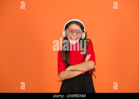 Accessoire de fête. Fille avec lunettes arrière-plan orange. Événement et divertissement. Fille de fête. Amuse-toi bien. Liste de lecture pour la fête. Concept de musique. Enfant porter des lunettes. Magasin de mode de lunettes. Piste froide. Banque D'Images