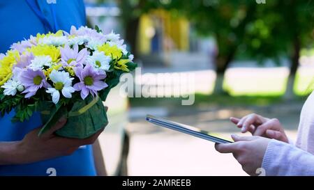 Client de la société de livraison ajoutant la signature sur le comprimé et recevant des fleurs Banque D'Images