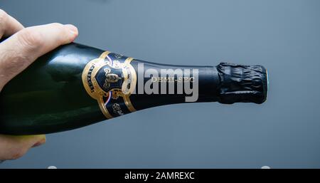 Paris, France - 1 janvier 2020: Main de l'homme tenant horizontalement une bouteille de vin mousseux Cremant d'Alsace sur fond bleu Banque D'Images