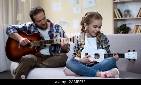 Père avec guitare et fille avec ukulele jouant la chanson, répétition de compétition Banque D'Images