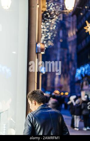 Strasbourg, France - 20 décembre 2016 : vue arrière de l'homme regardant par la vitrine du magasin de mode à la recherche d'un cadeau avec bokeh défocused en arrière-plan Banque D'Images