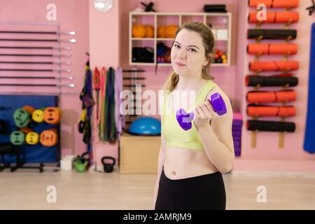 une jeune femme mince qui a récemment commencé à faire de l'exercice est engagée dans la salle de gym, commence des exercices avec des haltères Banque D'Images