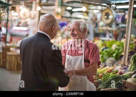 Un épicier adulte senior qui parle à un homme d'affaires dans un marché. Banque D'Images