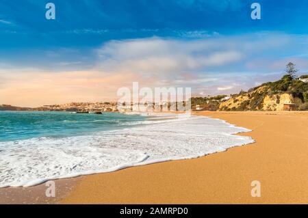 Mousse à vagues sur la plage de sable dans le village de la station balnéaire d'Albufeira, destination touristique populaire en Algarve, Portugal. Plage étendue Praia de Albufeira et sable blanc Banque D'Images