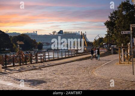 Un bateau de croisière se trouve au port de la ville côtière Baltique de Warnemunde Rostock, en Allemagne, tandis que le soleil se couche sous un ciel coloré et les touristes se promenent à pied Banque D'Images