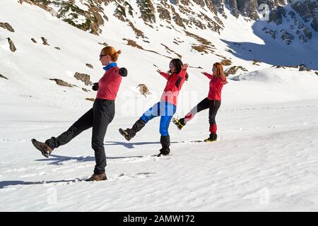 Trois femmes qui font un équilibre synchrone posent sur la neige, lors d'une journée d'hiver ensoleillée dans les montagnes de Bucegi, en Roumanie. Concept pour les activités de plein air amusantes. Banque D'Images