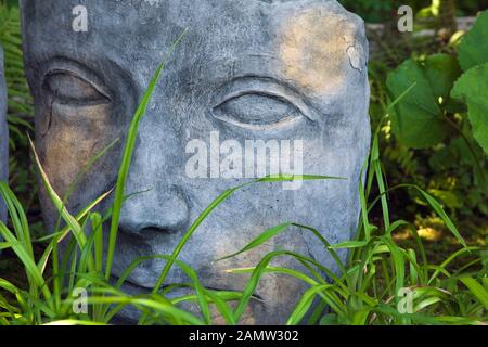 Gros plan d'une grande sculpture sur le visage dans un jardin résidentiel paysager en été, jardin de l'art du jardin, Saint-Laurent, Ile d'Orléans, Qc. Banque D'Images