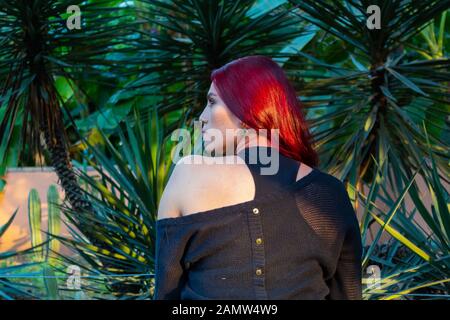 Jeune femme rousse hispanique portant des vêtements noirs, de l'arrière recevant la lumière du soleil au coucher du soleil réflexion Banque D'Images