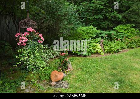 Pelouse et bordure d'herbe verte avec plantes Hosta et panier en fer forgé suspendu en forme de couronne avec fleurs roses Begonia semperflorens et Hedera. Banque D'Images