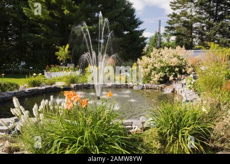 Étang avec fontaine bordée de Liatris spicata blanc - étoile étincelante, orange Hemerocallis - Daylily, Persicaria polymorpha - Giant Fleece fleurs Banque D'Images