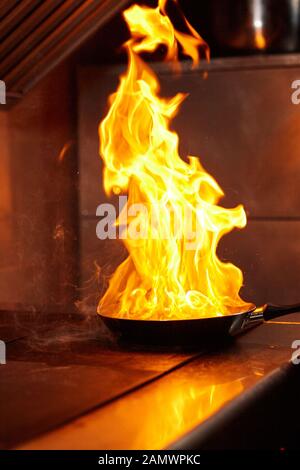 Flambe. Feu dans la poêle à frire. Chef professionnel dans une cuisine commerciale. Faites frire des aliments dans une poêle moulante sur la table de cuisson dans la cuisine extérieure Banque D'Images