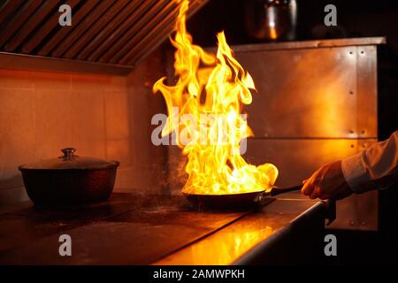 Flambe. Feu dans la poêle à frire. Chef professionnel dans une cuisine commerciale. Faites frire des aliments dans une poêle moulante sur la table de cuisson dans la cuisine extérieure Banque D'Images