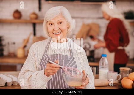 Une dame souriante à poil gris dans un tablier est positive Banque D'Images