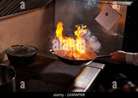 Flambe. Feu dans la poêle à frire. Chef professionnel dans une cuisine commerciale. Faites frire des aliments dans une poêle moulante sur la table de cuisson dans la cuisine extérieure Banque D'Images