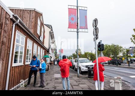 Reykjavik, Islande - 19 juin 2018 : les touristes de la rue avec parasol rouge et poncho sur le trottoir dans le centre-ville pluvieux jour nuageux Banque D'Images