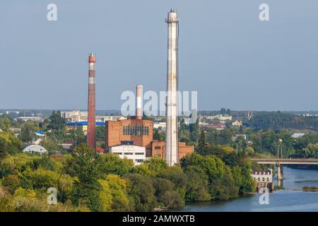 Centrale thermique de briques rouges avec de grands tuyaux d'échappement dans les arbres avec rivière, pont et ville au contexte le jour ensoleillé, ciel bleu. Bâtiments industriels et urbains concept vues Banque D'Images