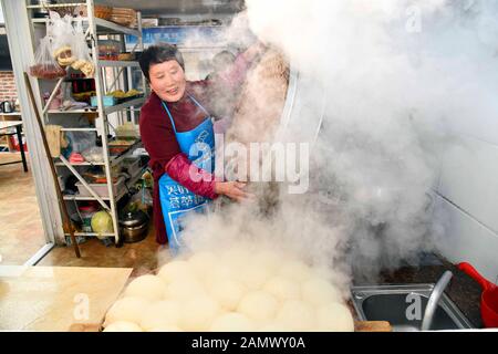 (200115) -- RONGCHENG, 15 janvier 2020 (Xinhua) -- Zhao Jinlan, la mère de Yu Haiyang, prépare des petits pains cuits à la vapeur dans la cuisine du village de Yandunjiao de Rongcheng, dans la province de Shandong, en Chine orientale, 12 janvier 2020. Yandunjiao, un village côtier de Shandong, est plein de vitalité autant de cygnes hivernent ici. Fin 2014, le service de train à grande vitesse entre Qingdao et Rongcheng a été lancé et de nombreux touristes sont venus ici pour voir les cygnes, goûter les spécialités locales et découvrir la famille d'accueil dans les maisons au toit d'algues. Yu Haiyang, un villageois natif qui a travaillé une fois à Singapour après son diplôme, est revenu à ho Banque D'Images