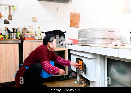 (200115) -- RONGCHENG, 15 janvier 2020 (Xinhua) -- Zhao Jinlan, la mère de Yu Haiyang, prépare des petits pains cuits à la vapeur dans la cuisine du village de Yandunjiao de Rongcheng, dans la province de Shandong, en Chine orientale, 12 janvier 2020. Yandunjiao, un village côtier de Shandong, est plein de vitalité autant de cygnes hivernent ici. Fin 2014, le service de train à grande vitesse entre Qingdao et Rongcheng a été lancé et de nombreux touristes sont venus ici pour voir les cygnes, goûter les spécialités locales et découvrir la famille d'accueil dans les maisons au toit d'algues. Yu Haiyang, un villageois natif qui a travaillé une fois à Singapour après son diplôme, est revenu à ho Banque D'Images