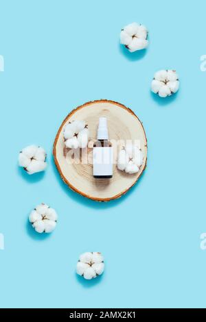 Concept zéro déchet. Flacon réutilisable en verre pour huile naturelle, parfum ou déodorant entouré de fleurs de coton sur une découpe en bois, plateau Banque D'Images