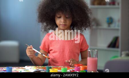 Petite fille africaine curieusement peindre une image et sourire, heureuse enfance Banque D'Images